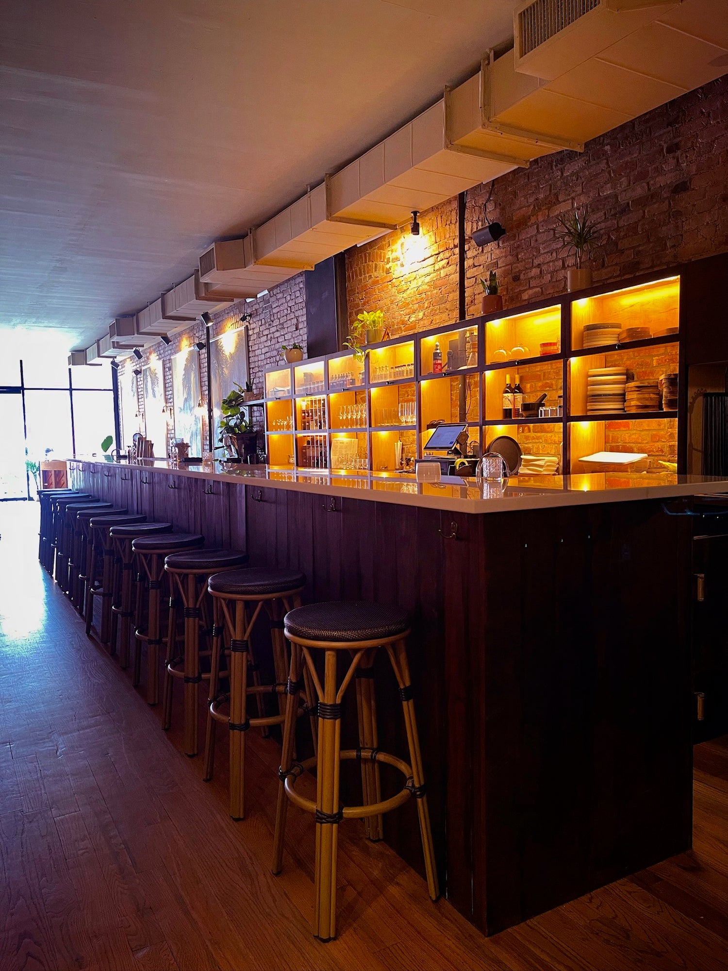 Bar area with wooden counter, stools, and shelves with bottles and glasses.