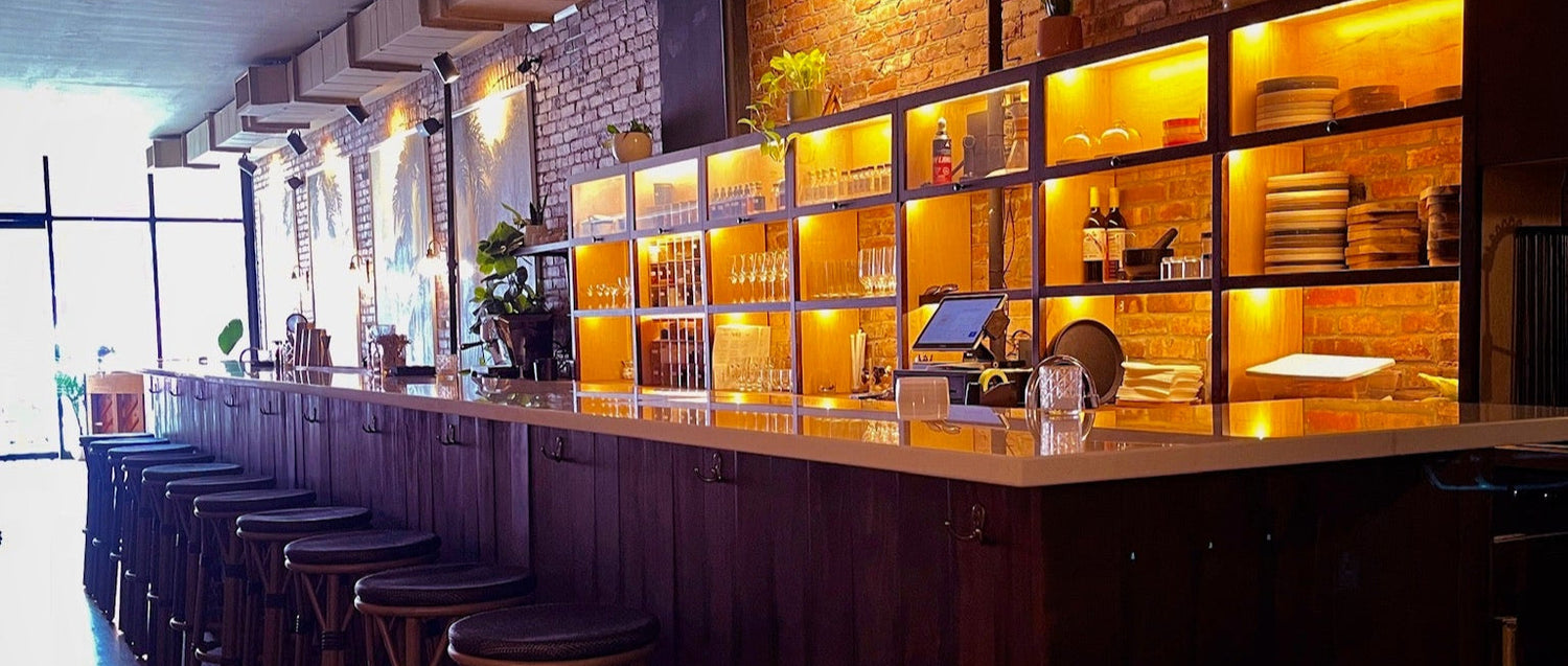 Bar area with wooden counter, stools, and shelves with bottles and glasses.