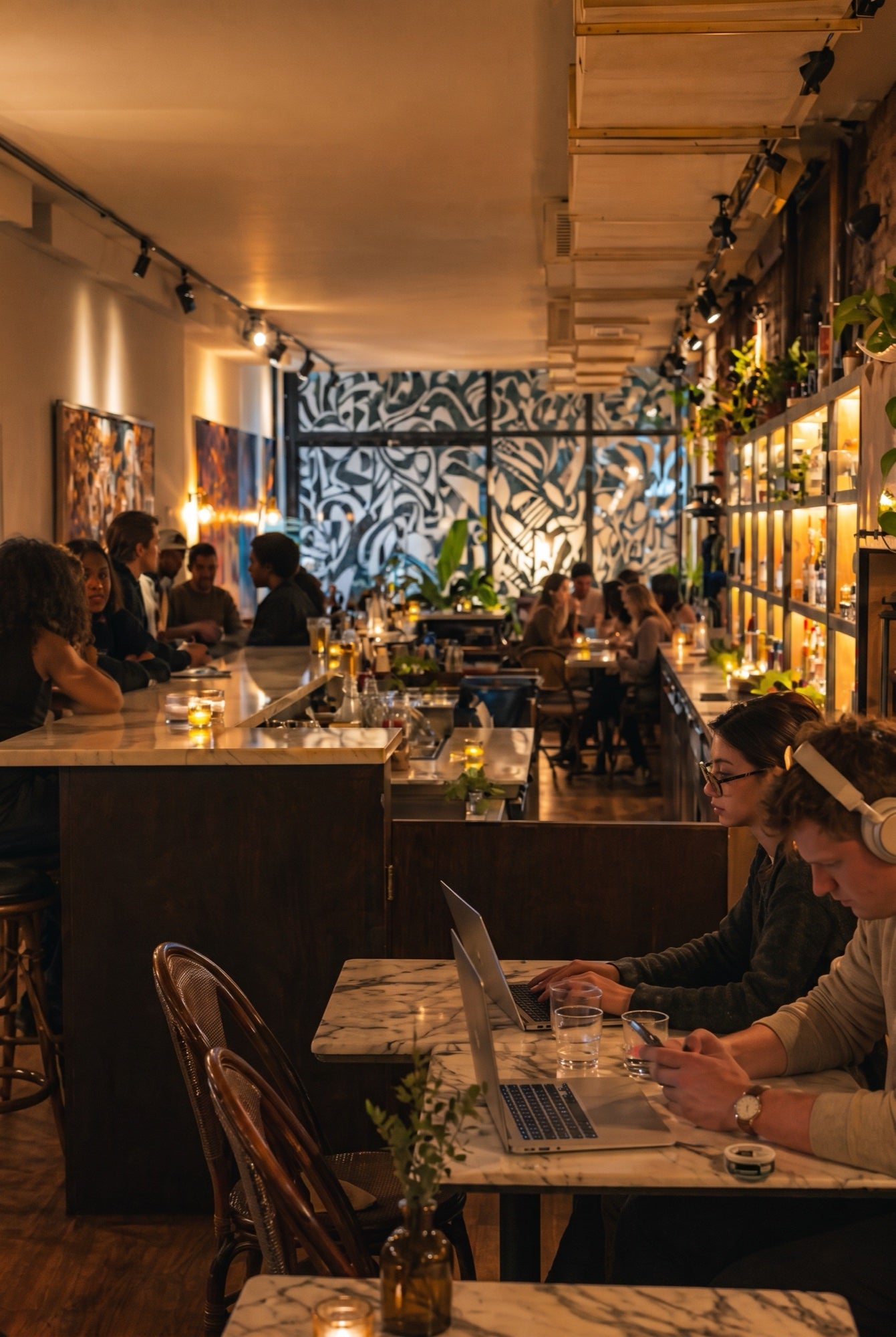 Guests working on laptops at a marble table along the bar at No More Cafe in the evening