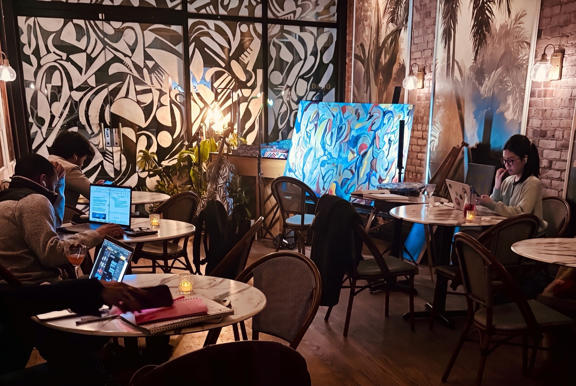 Guests on laptops at candlelit tables in the mural room at No More Cafe at night